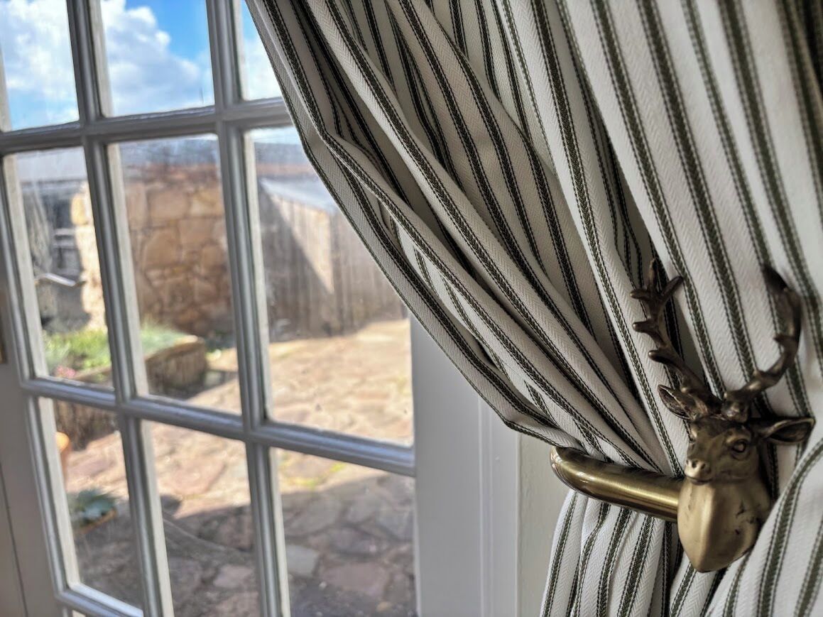 A window with a view of a stone wall and a metal deer head curtain rod.