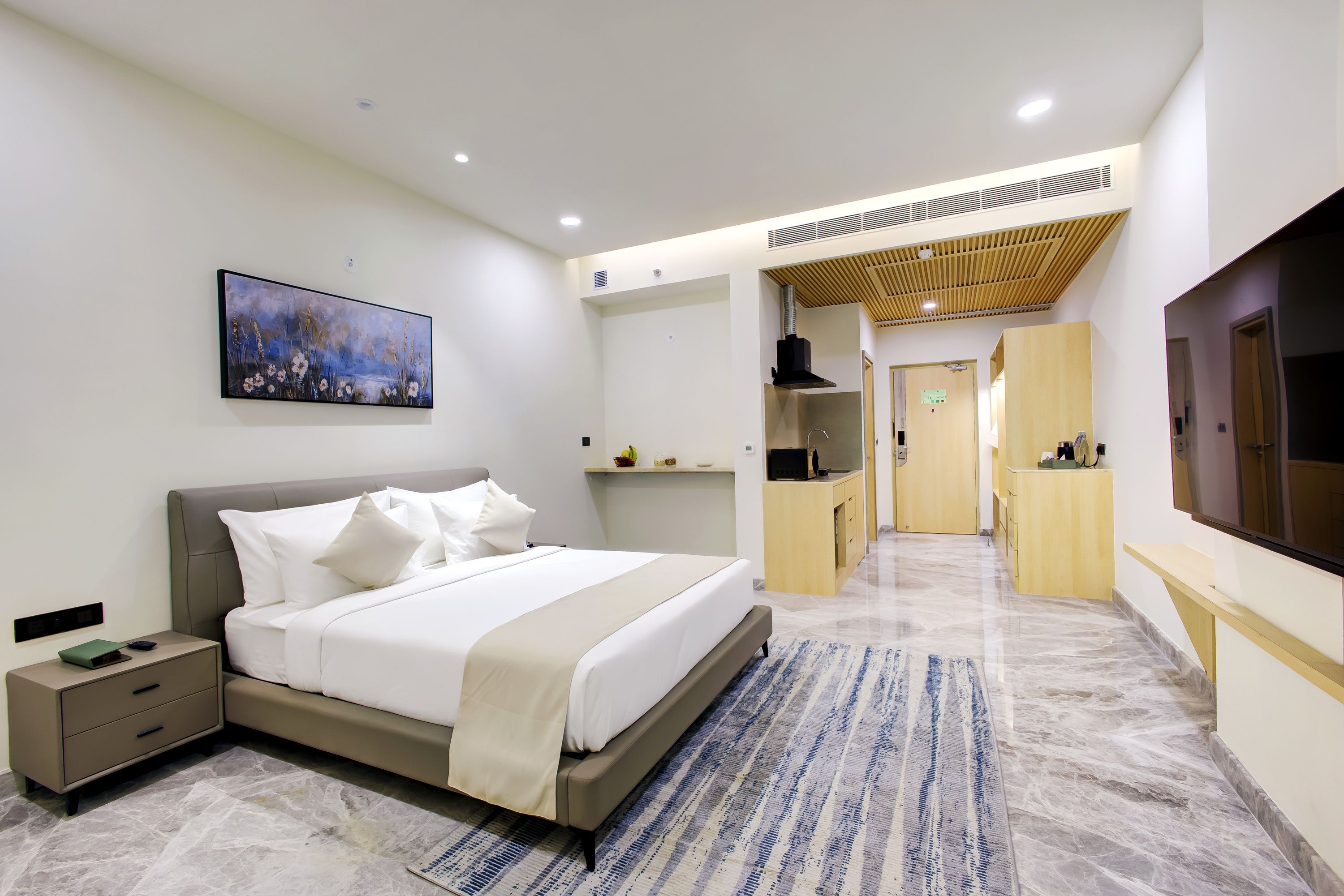 A modern hotel room with a bed, bedside table, artwork, and a TV.