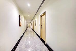 A long, narrow hallway with doors on both sides, each marked with a number. The floor is tiled with a marble pattern. - Cygnett Collection (Gurugram)