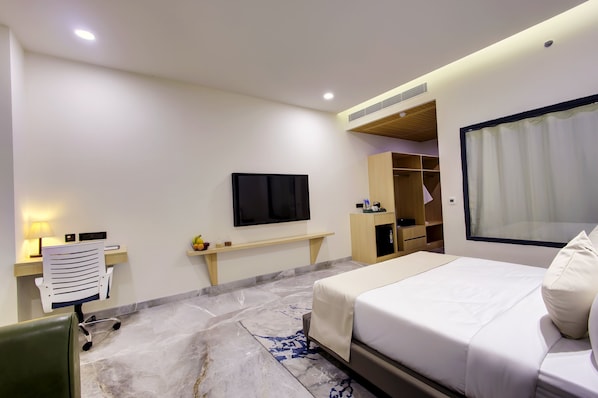 A hotel room with a bed, a desk with a lamp, a TV, a wardrobe, and a window with curtains. - Cygnett Collection (Gurugram)