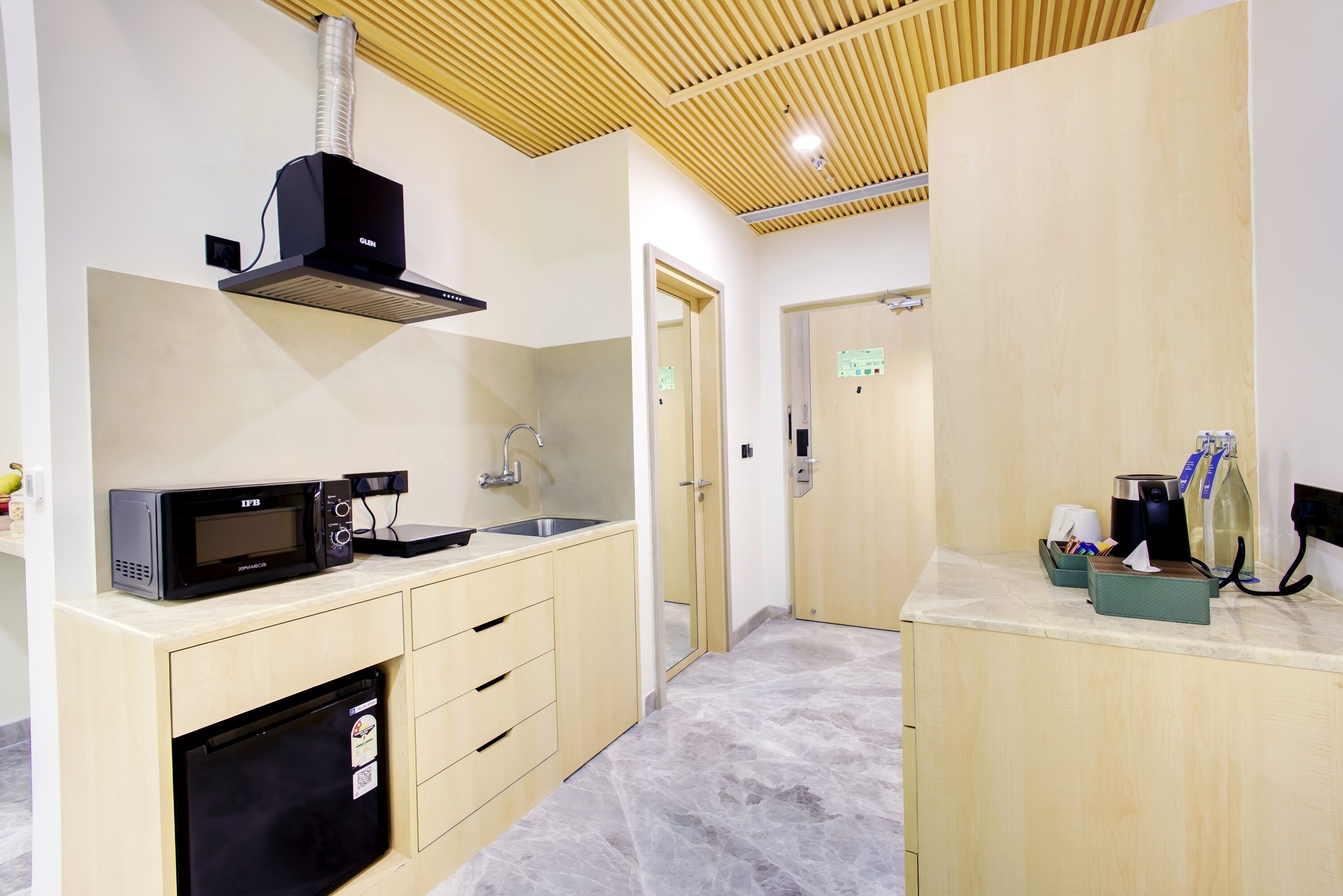 Een moderne keuken met een ingebouwde magnetron, een koffiezetapparaat en een kleine koelkast.