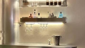 A bar area with two chairs, a shelf with bottles and glasses, and a lighted shelf above.