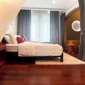 Ein Schlafzimmer mit Bett, Nachttisch, einem Fenster mit Vorhängen und einem kleinen Tisch mit Stuhl.