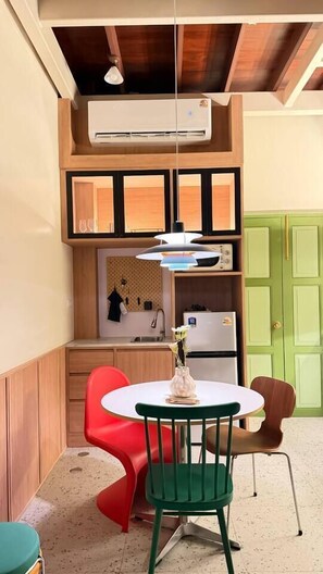 A compact kitchen with a built-in air conditioner, a small dining area with a round table and chairs, and a green door in the background. - Nueng Rana 149 | A Unique Stay Experience | BKK - Holiday Home (Samphanthawong)