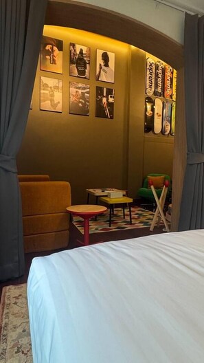 Habitación de hotel con cama, sofá, una mesita y una silla. Cuadros enmarcados adornan la pared.
