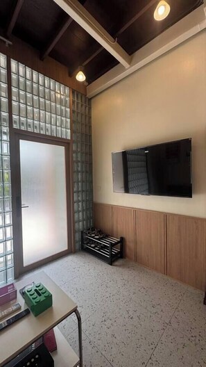 A room with a television mounted on the wall, a sliding glass door, and a small table with a remote control. - Nueng Rana 149 | A Unique Stay Experience | BKK - Holiday Home (Samphanthawong)