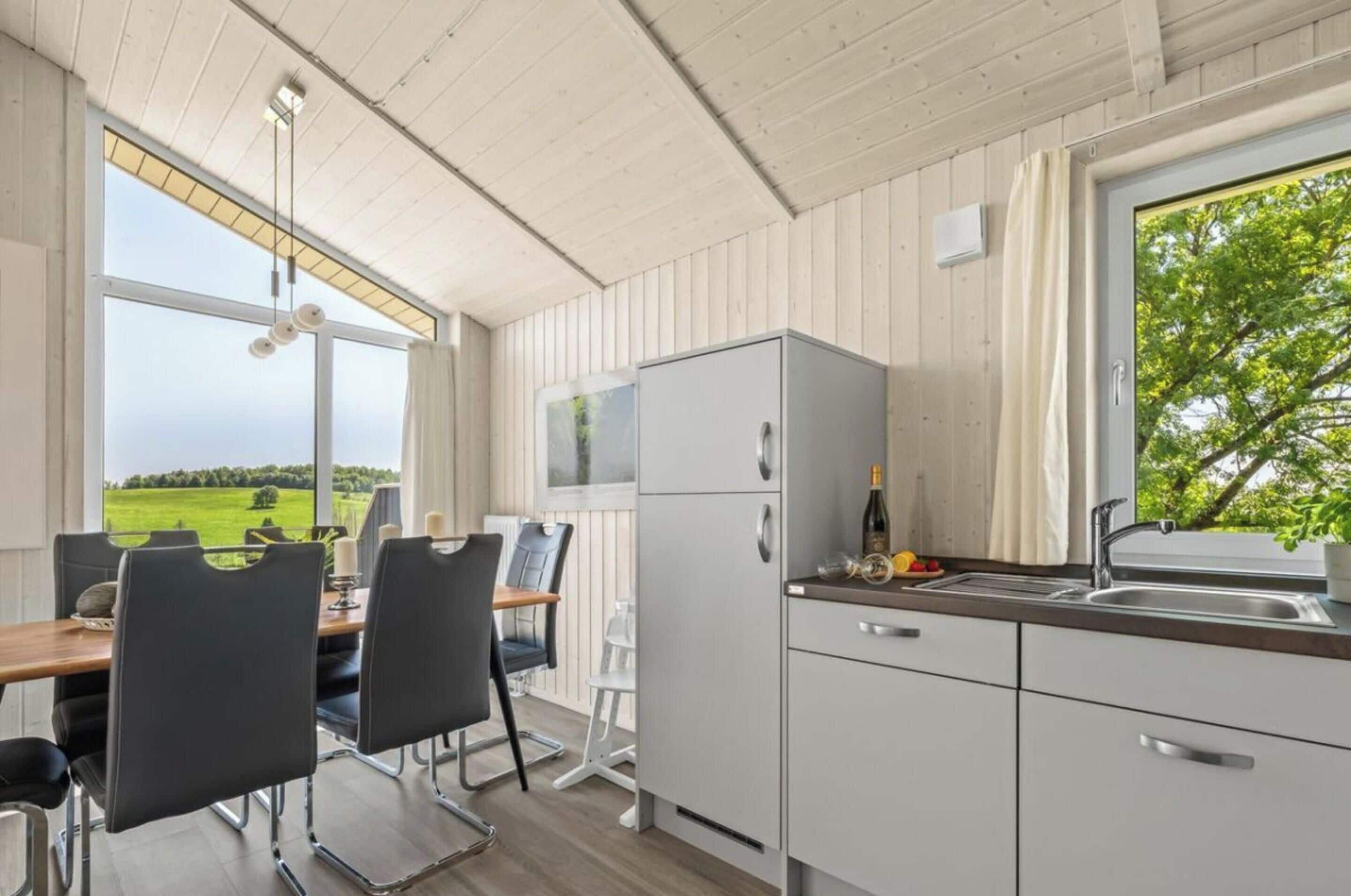A modern kitchen with a view of a green landscape, a dining area with chairs, and a window with curtains.