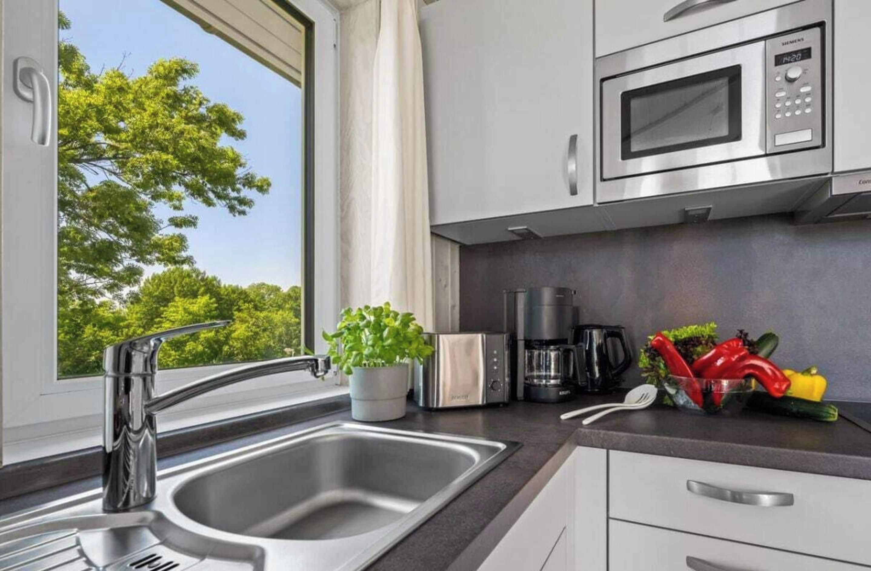 Een moderne keuken met een RVS spoelbak, een magnetron en een koffiezetapparaat.