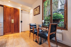 A room with a wooden door, a glass table with chairs, a radiator, and a window with a view of greenery. - luxury 1BR quiet fully equipped kitchen washer/drier (Paris)