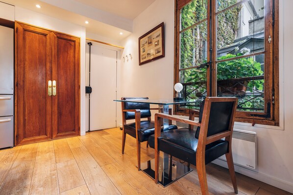 Une pièce avec une porte en bois, une table en verre entourée de chaises, un radiateur et une fenêtre donnant sur un paysage verdoyant.