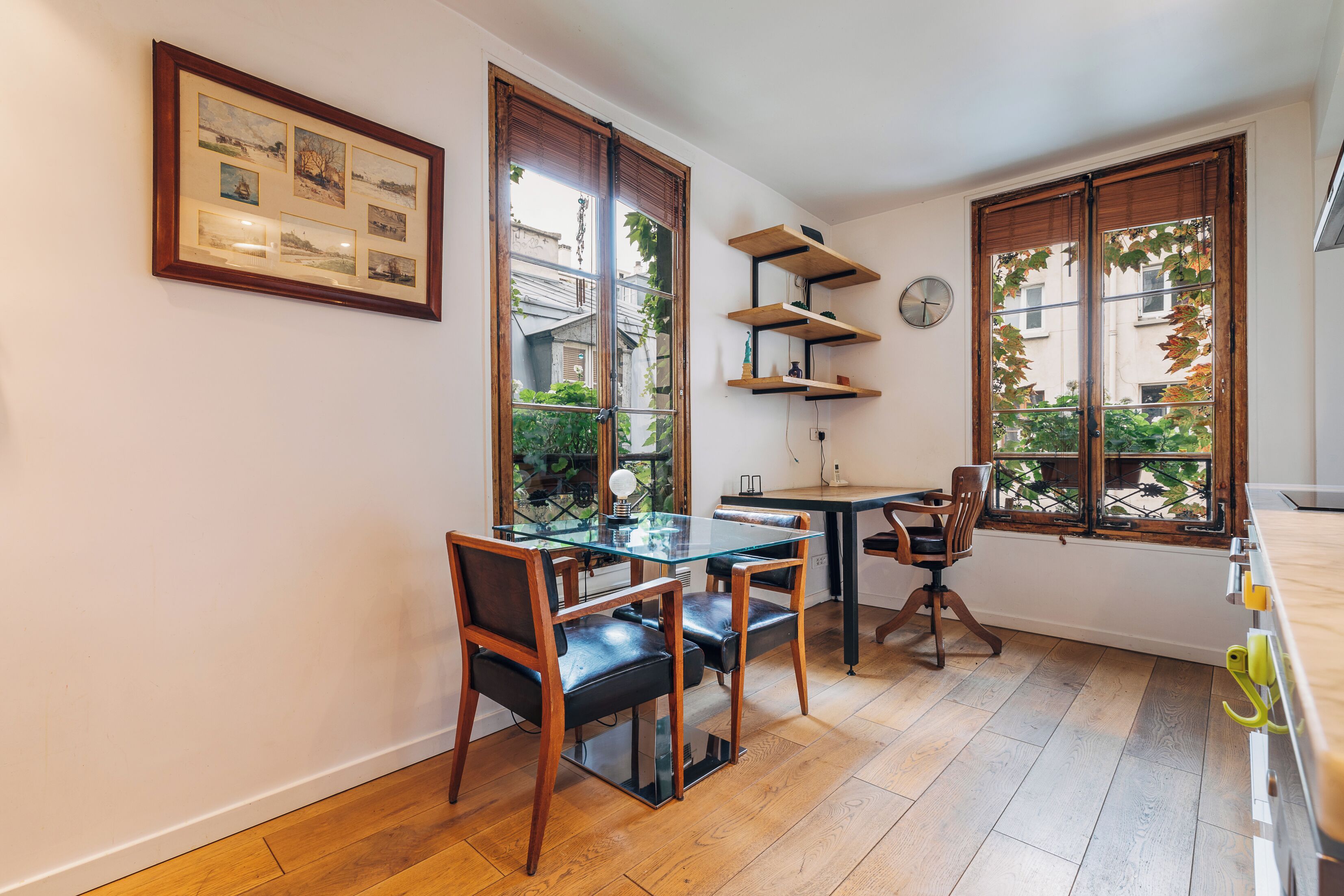Un comedor con mesa y sillas de vidrio, estanterías de madera y ventanas amplias con vistas al follaje.