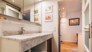 Un baño moderno con lavamanos de mármol, un espejo y obras de arte enmarcadas en la pared.