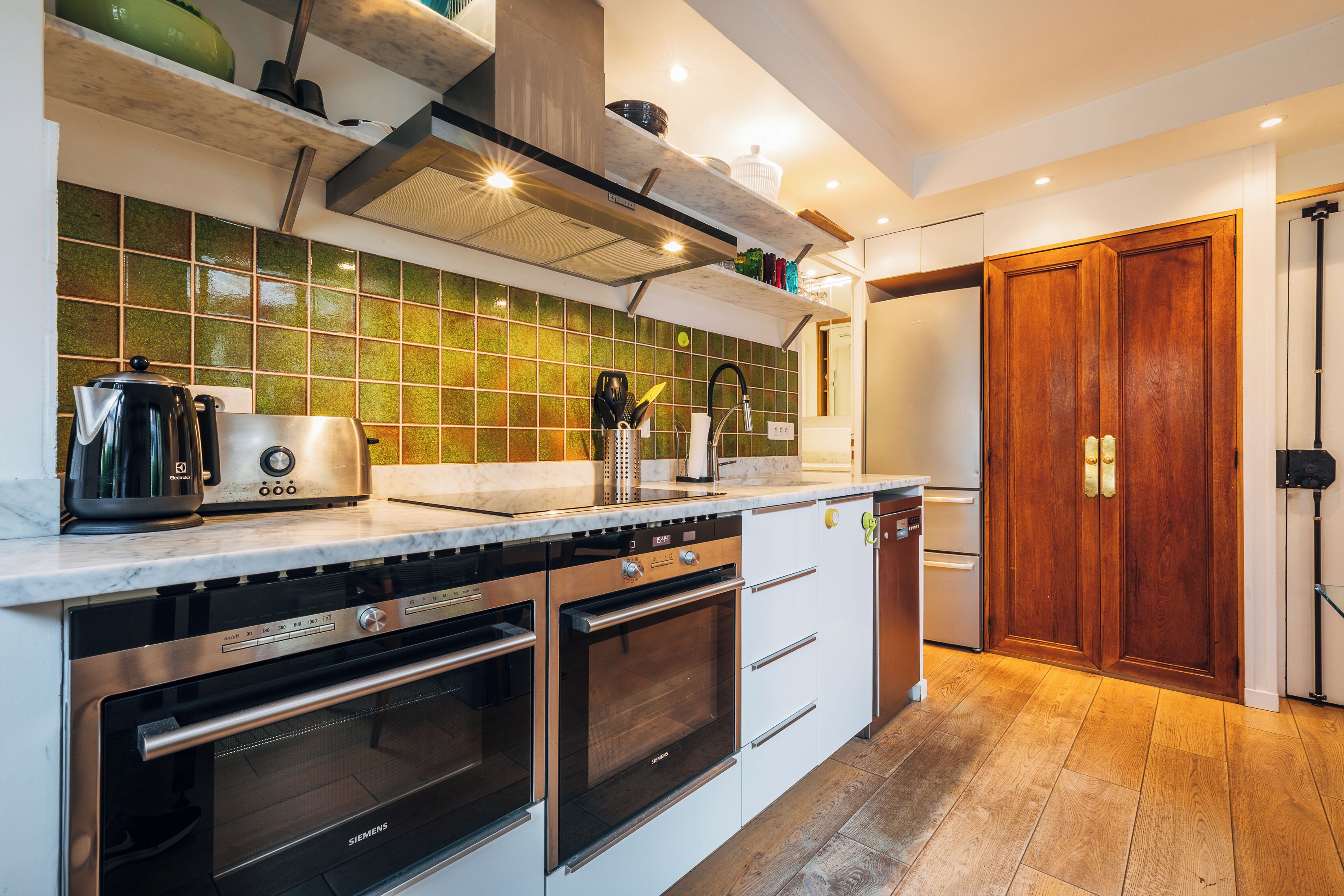 A modern kitchen with stainless steel appliances, a marble countertop, and a green-tiled backsplash.