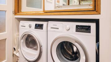 A laundry room with two front-loading washing machines, a wooden-framed mirror above them, and a wooden floor.