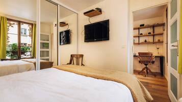 A bedroom with a bed, a television mounted on the wall, a desk with a chair, and a sliding door leading to a balcony.