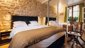 Un dormitorio con pared de piedra, una cama grande con ropa de cama blanca, una mesita de noche de madera y una silla.