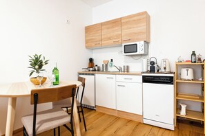 A compact kitchen with white cabinets, a microwave, a dishwasher, and a dining area with a table and chairs. - Ardell - Aceessible Location - Comfortable 1BR - FREE Garage (Vienna)