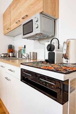 A modern kitchen with white cabinetry, a built-in microwave, a kettle, and a coffee maker. - Ardell - Aceessible Location - Comfortable 1BR - FREE Garage (Vienna)