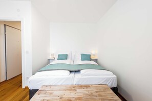 A bedroom with a bed, bedside lamps, a wooden table, and a door. - Ardell - Aceessible Location - Comfortable 1BR - FREE Garage (Vienna)