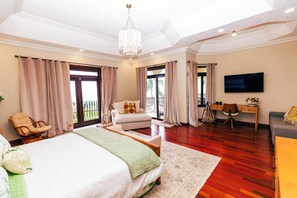 A spacious bedroom with a large bed, a sitting area with a chair, a desk, and a television. - Luxury 6-bedroom estate in charming Ocho Rios overlooking the Caribbean Sea (Ocho Rios)