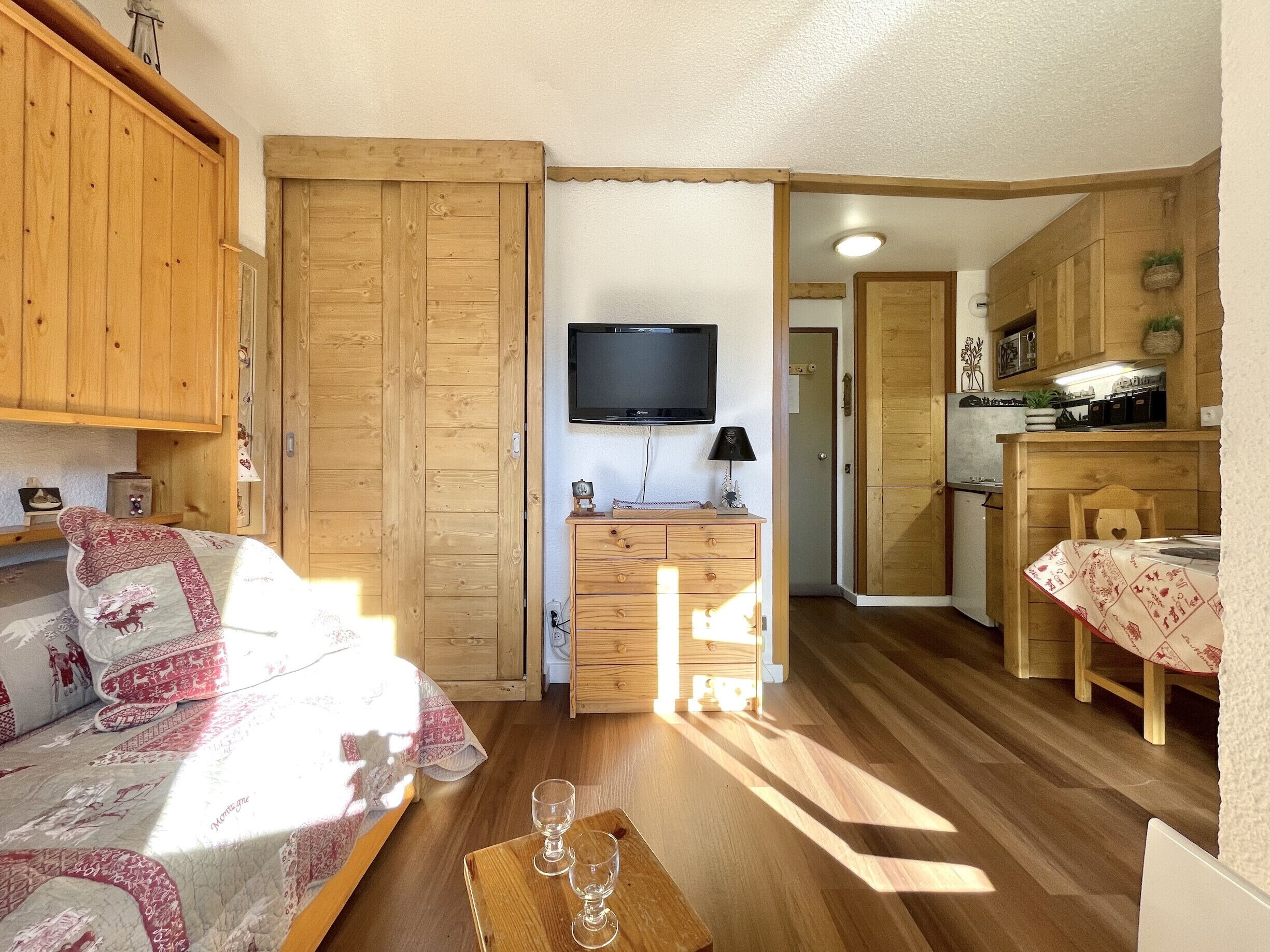 Een gezellige kamer met een bed, een houten garderobe, een televisie, een bureau met een lamp en een kitchenette.