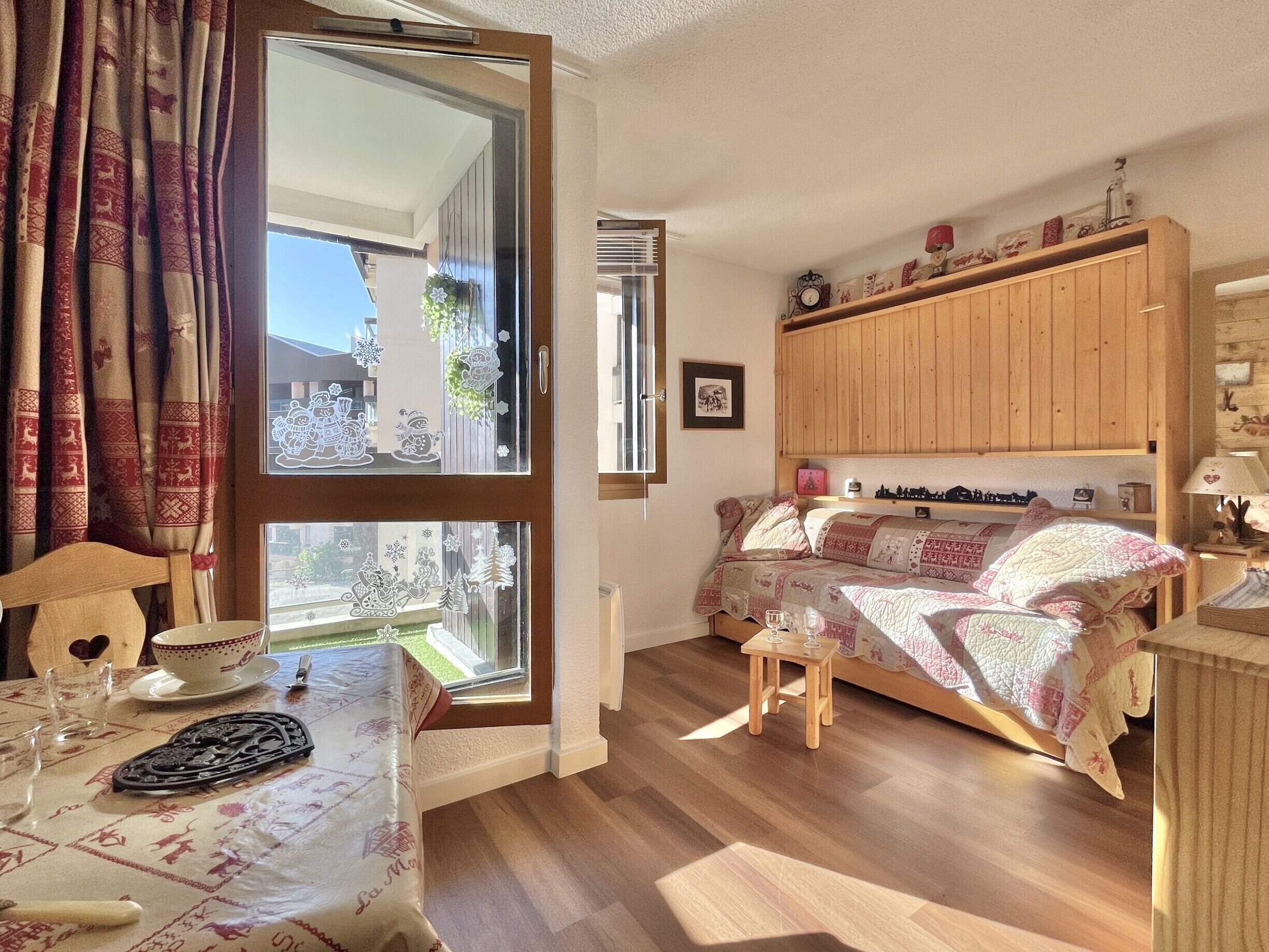 Une pièce confortable avec un lit, une armoire en bois, une table recouverte d’une nappe et une fenêtre avec des rideaux.