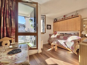 Une pièce confortable avec un lit, une armoire en bois, une table recouverte d’une nappe et une fenêtre avec des rideaux.