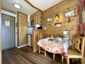 A wooden interior with a dining table set for two, a kitchen area, and a door with a notice. - (SO.317) Alpine-style studio, right at the slopes, Les (Les Menuires)