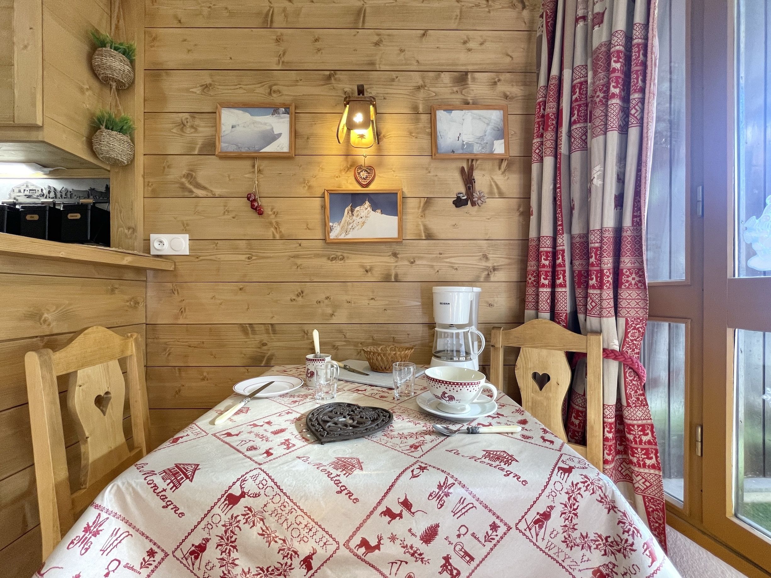 Interior em madeira com mesa posta para refeição, cafeteira e quadros nas paredes.