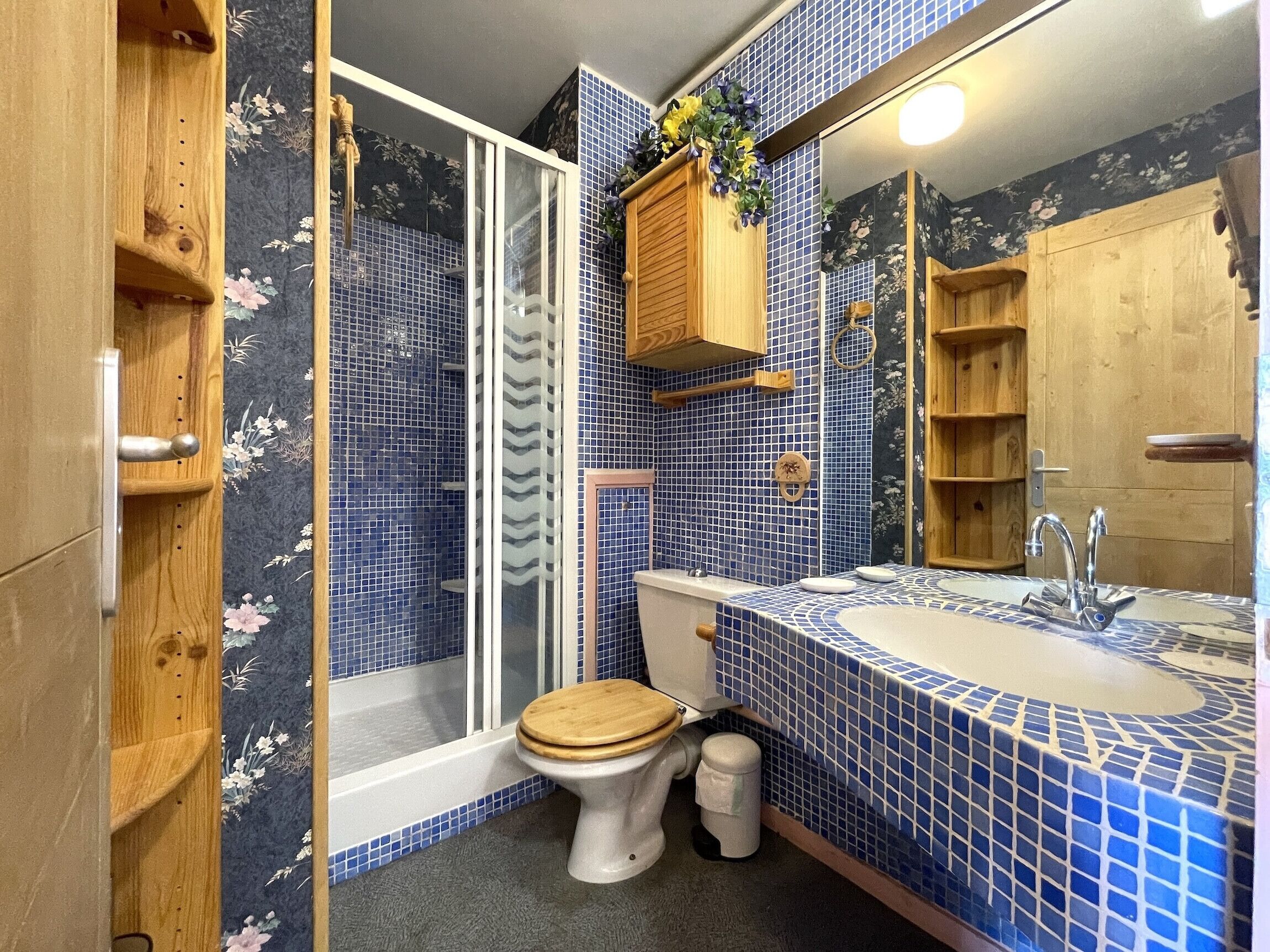 Baño con ducha, inodoro y lavabo, con mosaicos azules y detalles de madera.