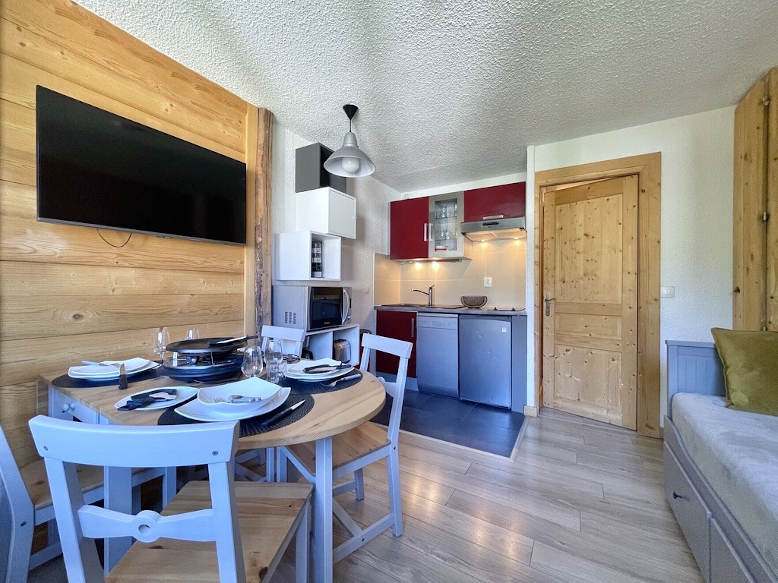 Cocina compacta con comedor, paredes de madera y televisor integrado.