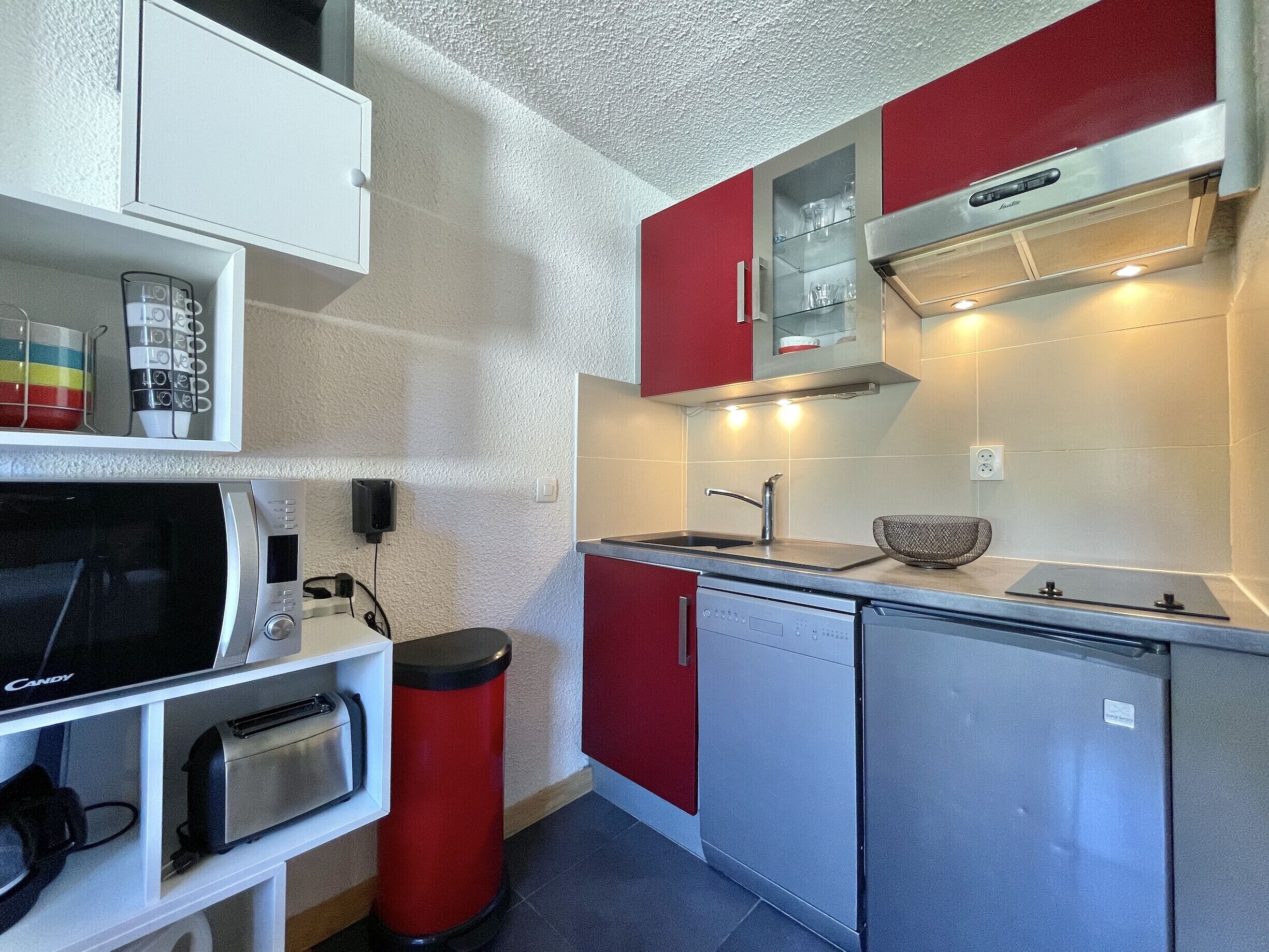 A compact kitchen with a microwave, toaster, sink, and red cabinets.