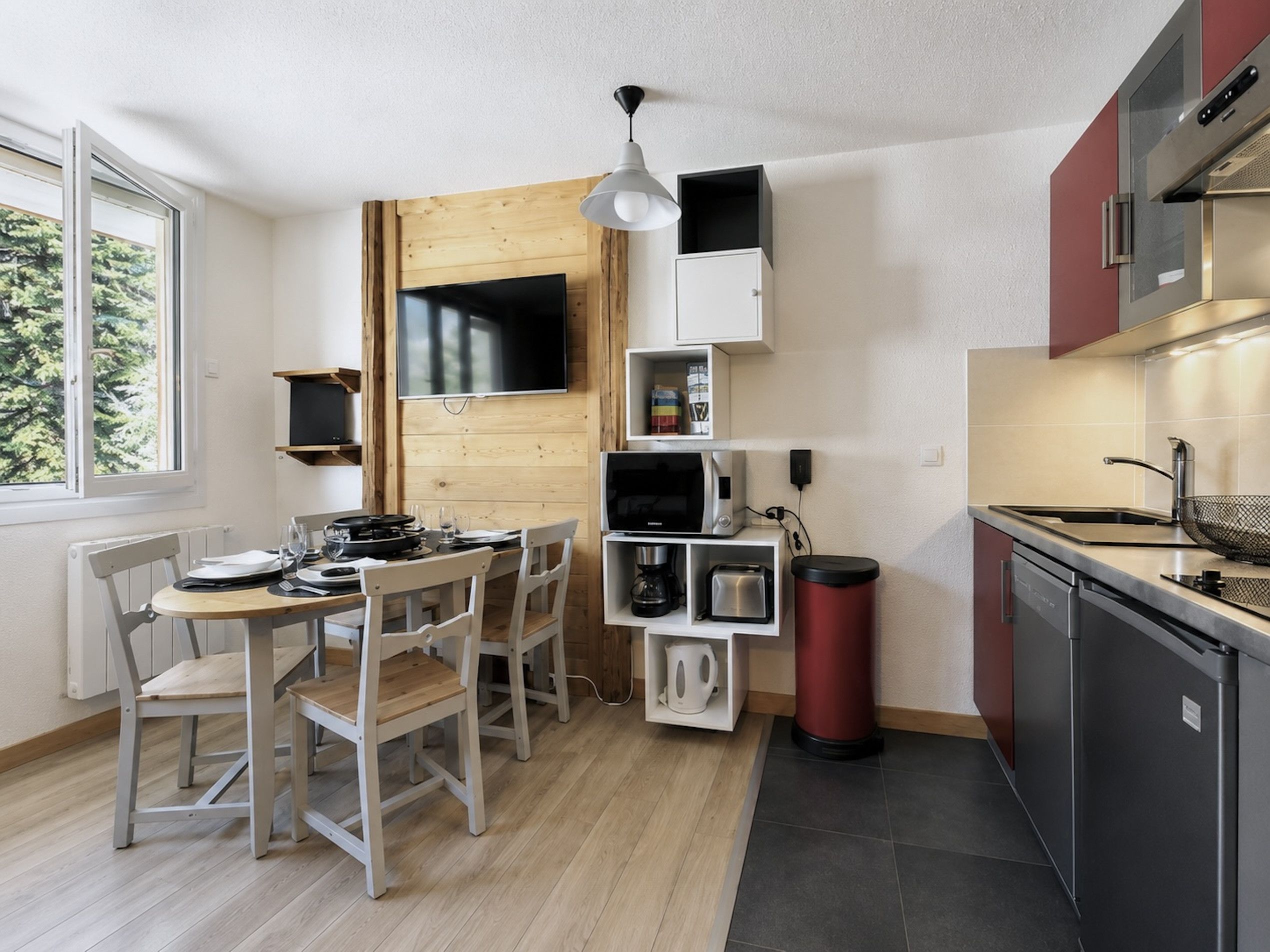 A compact kitchen with a dining area, a microwave, a coffee maker, and a trash bin.