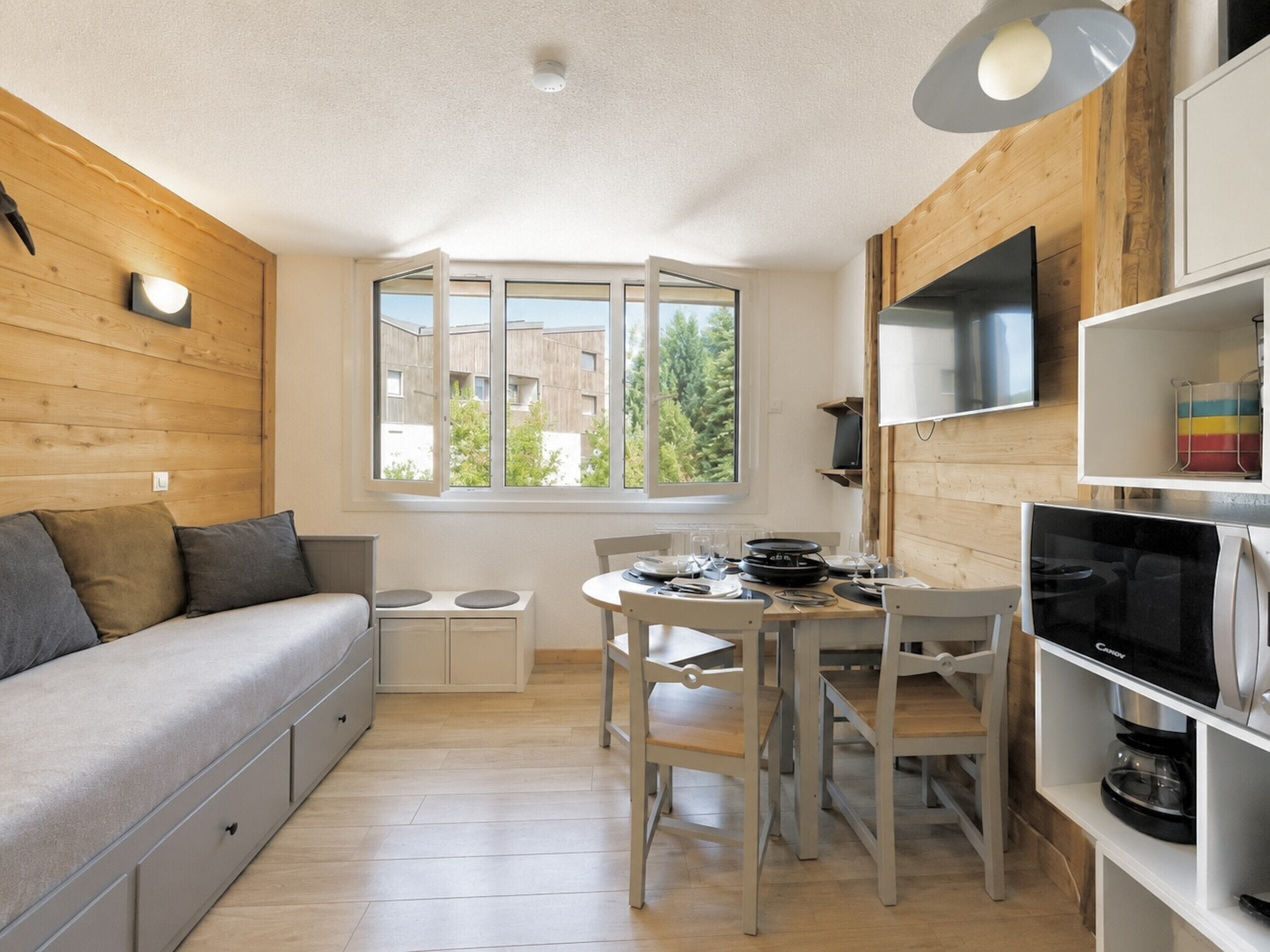 A compact living space with a sofa, dining table, chairs, and a TV on a shelf.