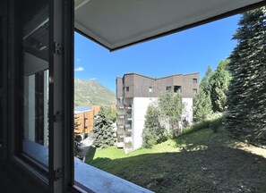 A view from a window overlooking a building with a sloped roof, surrounded by greenery and a mountain in the background. - (BO.421) Comfortable studio, right at the slopes in 3 Vallées (Les Menuires)