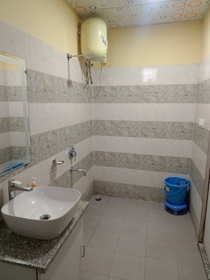 Un baño con lavamanos, espejo, ducha y un cubo azul.