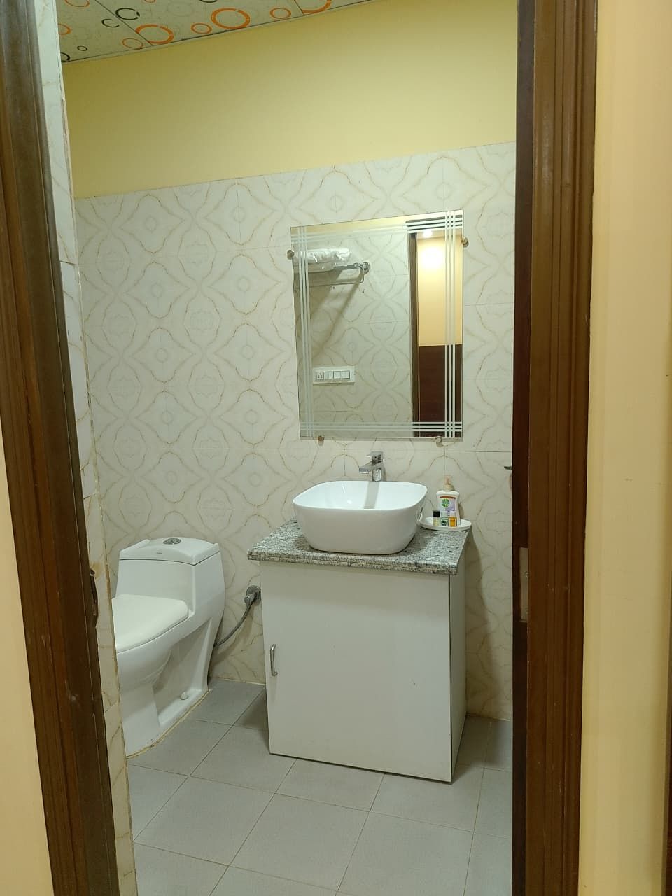 Un baño con un inodoro blanco, un lavamanos con un espejo encima y una pared con diseño.