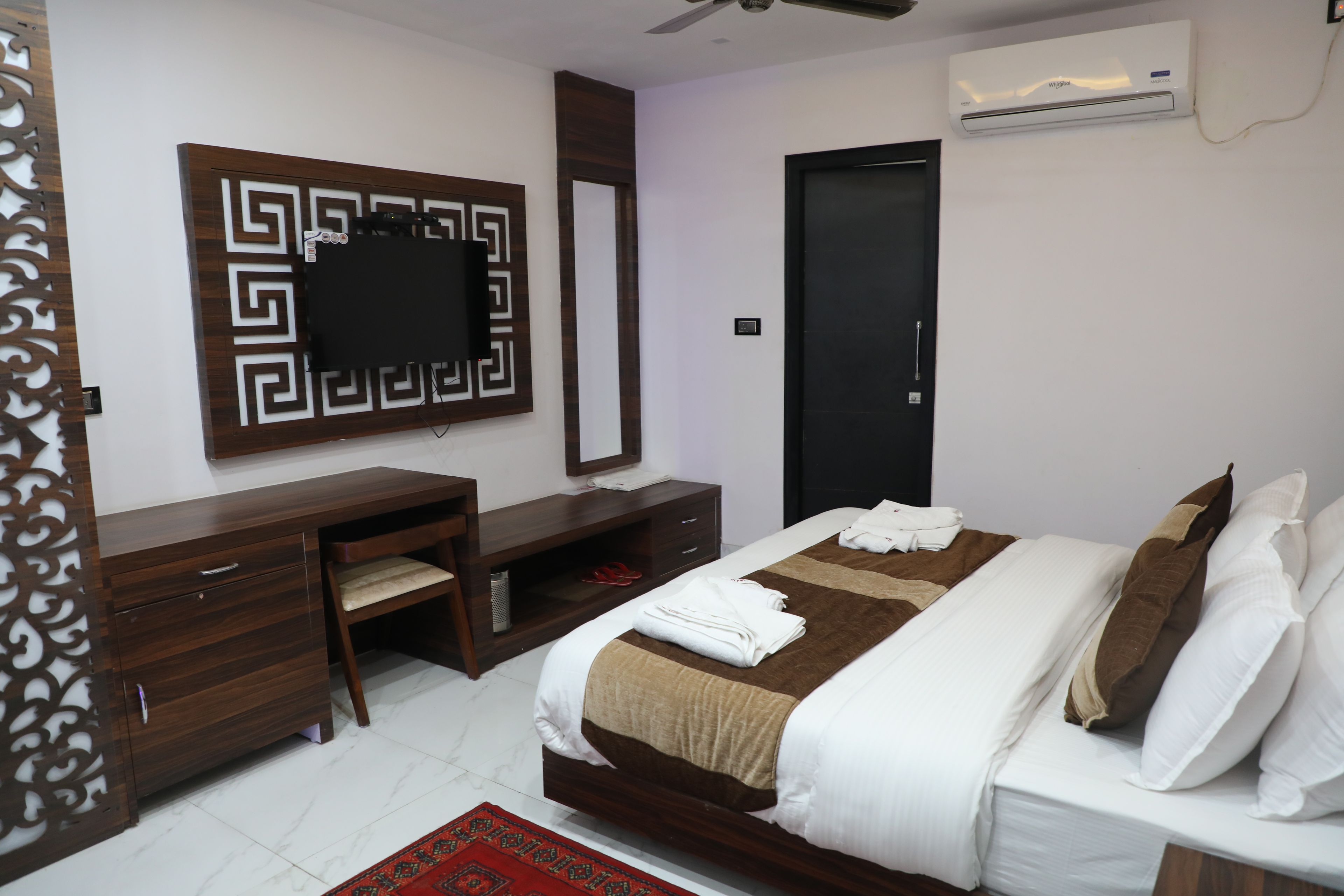 Habitación de hotel con cama, escritorio, silla, armario, espejo y aire acondicionado.