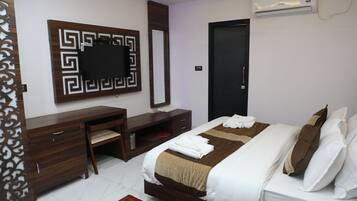 Habitación de hotel con cama, escritorio, silla, armario, espejo y aire acondicionado.