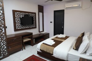 A hotel room with a bed, a desk, a chair, a wardrobe, a mirror, and an air conditioning unit. - Mix Grand Family Restaurant (Kotdwar)