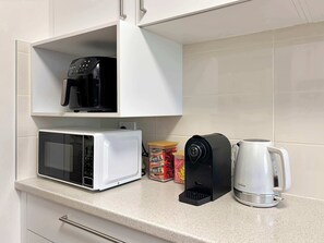 Una cocina con microondas, cafetera y hervidor sobre la encimera.