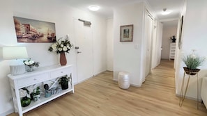 A hallway with a white console table, a vase of flowers, a painting, and a potted plant. - Style & Bright 2BR with leafy balcony & parking (Cammeray)