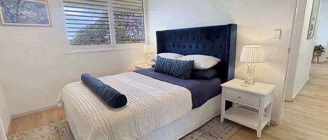 Un dormitorio con una cama, mesitas de noche, una lámpara y una ventana con persianas.