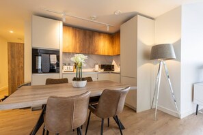 A modern kitchen with wooden cabinets, a dining table with chairs, and a floor lamp. - The Penthouse at No 162 (Birmingham)