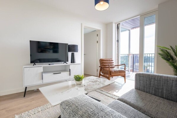 A modern living room with a flat-screen TV, a sofa, a coffee table, and a chair. - The Penthouse at No 162 (Birmingham)