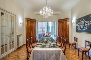 Ein Esszimmer mit einem langen Tisch, gedeckt für sechs Personen, flankiert von Holzschränken und Stühlen, einer Pendelleuchte und Blick durch Glastüren.