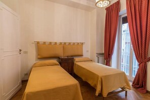 Quarto com duas camas de solteiro, cabeceira de madeira, mesa de cabeceira pequena e janela com cortinas vermelhas.
