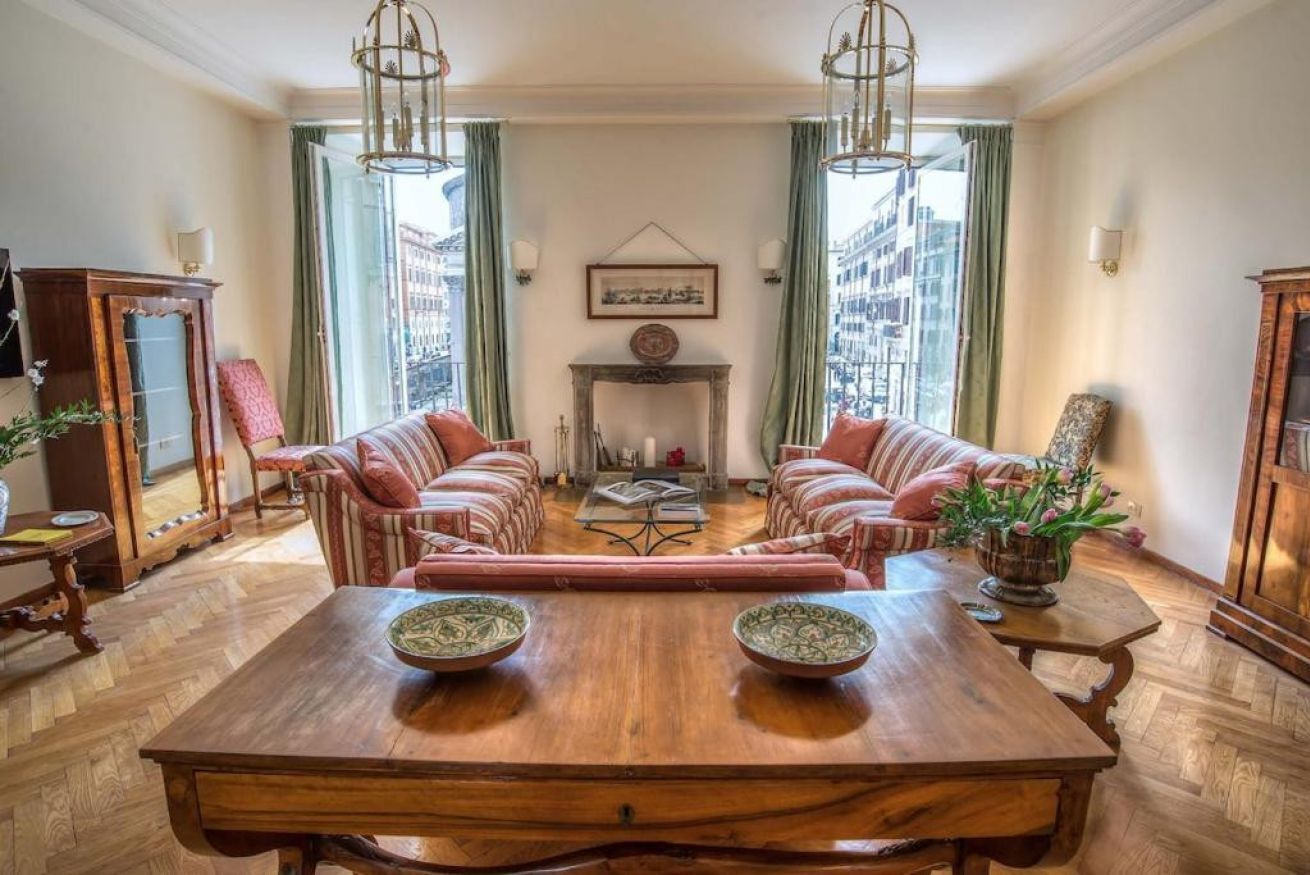 Een ruime woonkamer met een grote houten tafel, twee banken en een open haard.
