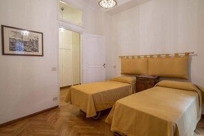 Ein Zimmer mit zwei Einzelbetten, Holzboden, einer weißen Tür und einem gerahmten Bild an der Wand.
