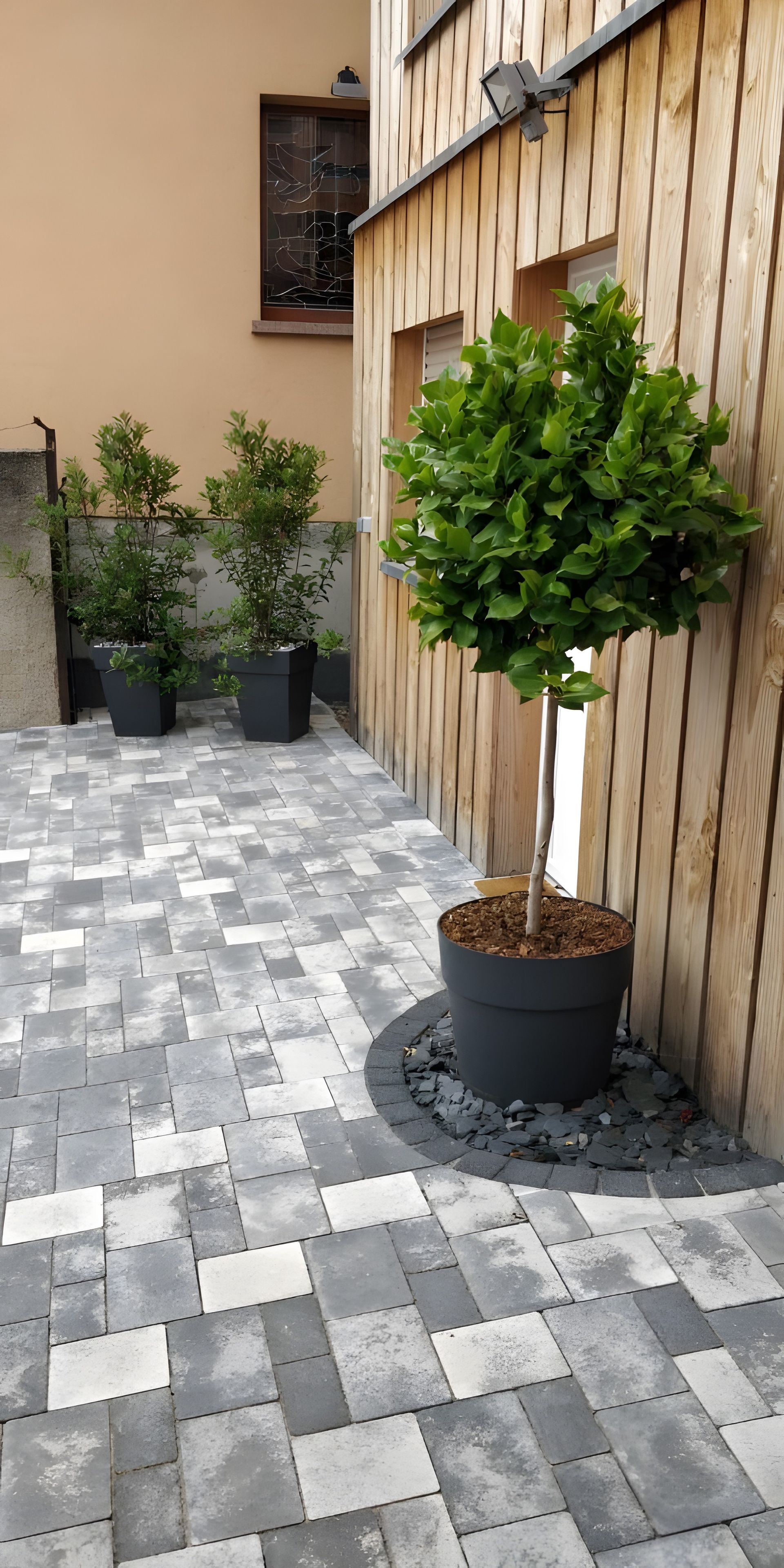Une terrasse dallée, agrémentée de plantes en pot et entourée d’une clôture en bois.